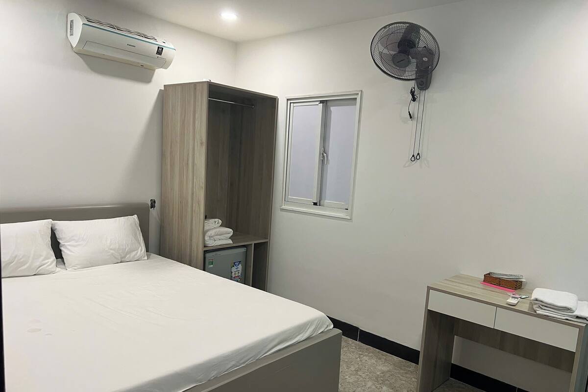 Une chambre bien rangée, avec un lit, une armoire, un bureau et un ventilateur.