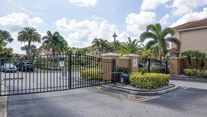 A gated parking area with palm trees and a building with a red-tiled roof.