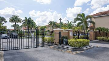 A gated parking area with palm trees and a building with a red-tiled roof.