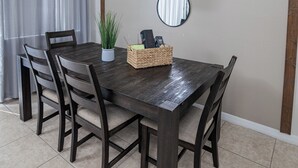 A dining area with a dark wooden table, four chairs, a potted plant, a basket, and three wall-mounted mirrors.