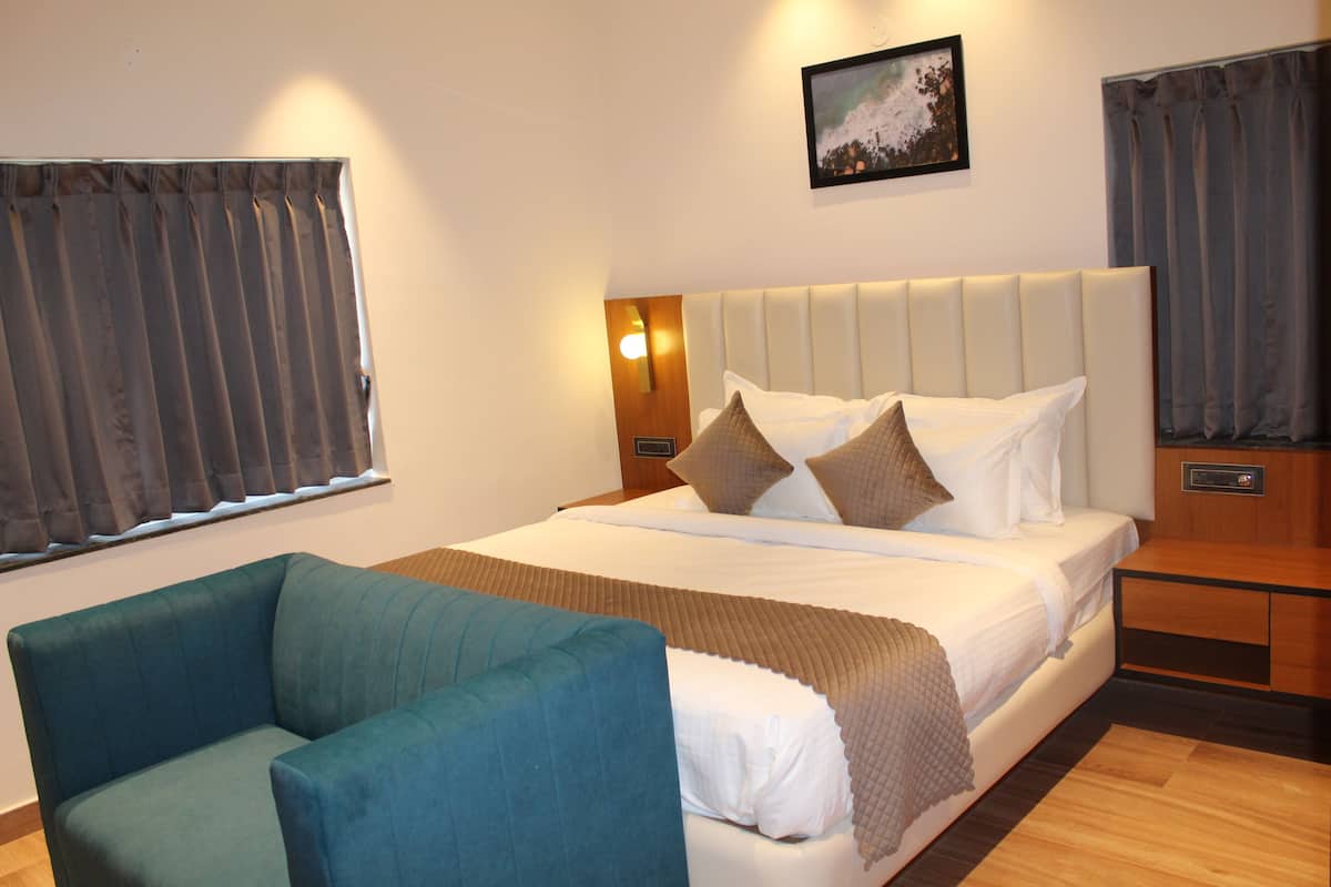 A hotel room with a bed, a blue armchair, a bedside table, and a wall-mounted picture.