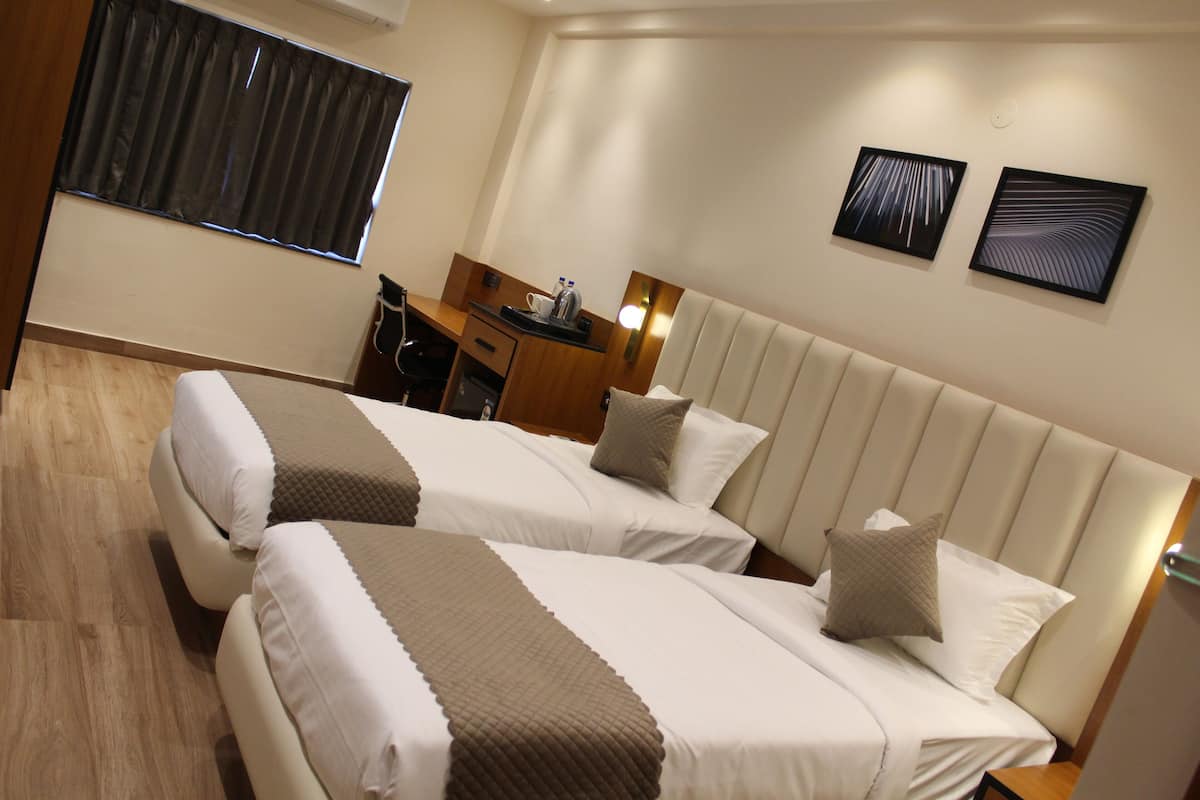 A hotel room with two beds, a desk, and a chair. There are two framed artworks on the wall.
