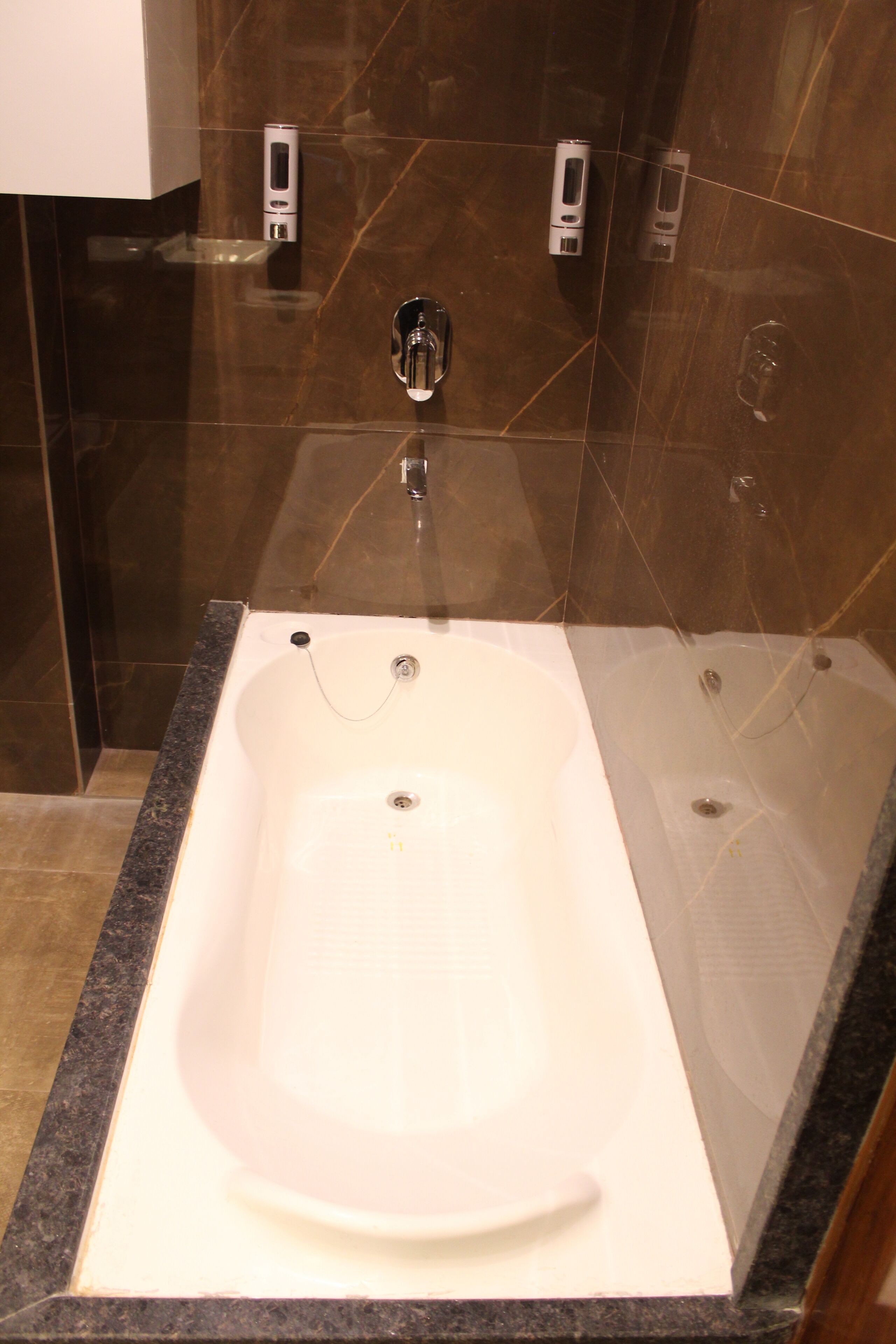 A modern bathroom with a large bathtub, marble walls, and a glass shower enclosure.