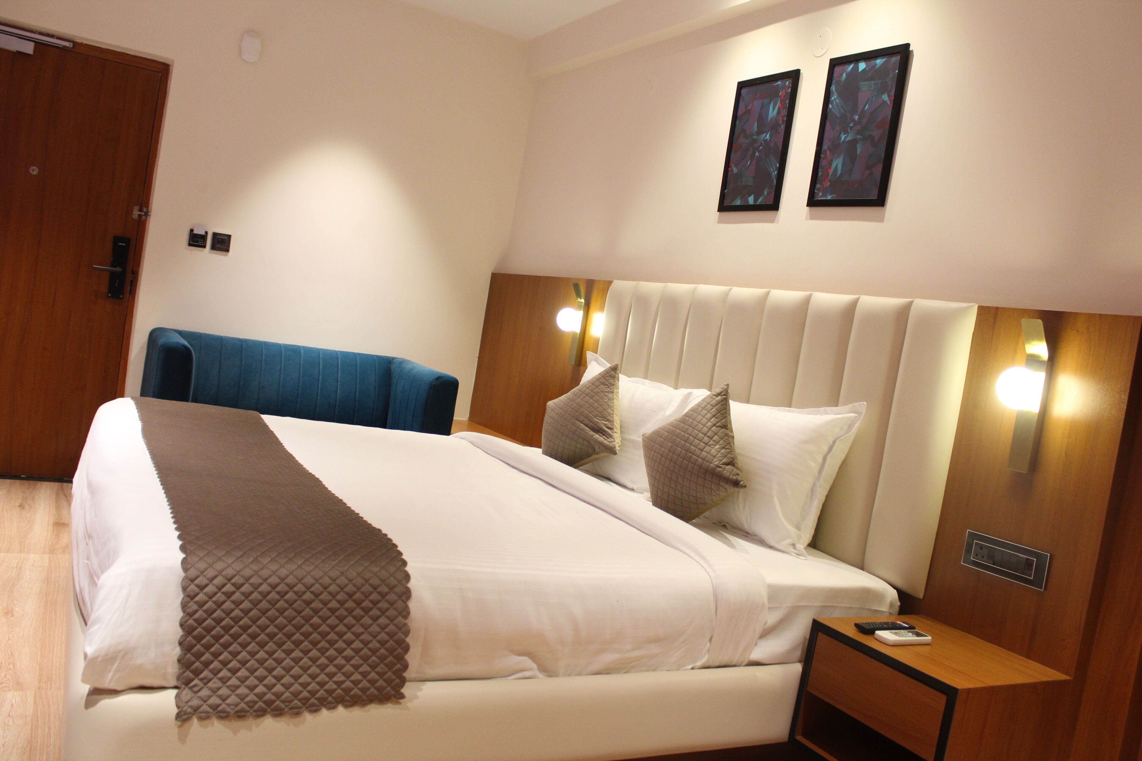 A hotel room with a large bed, a wooden nightstand, a blue chair, and two wall-mounted lights.
