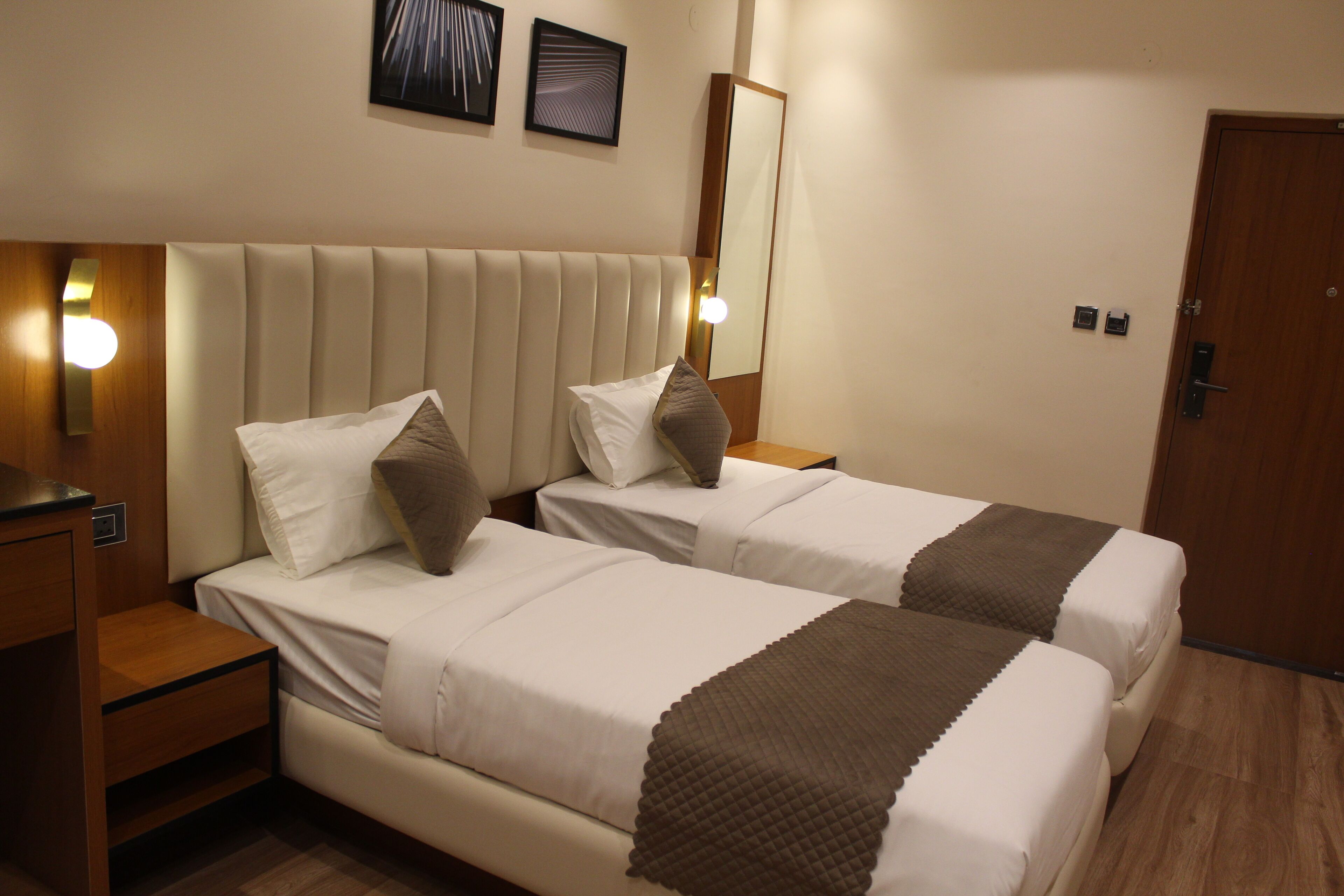A hotel room with two beds, a wooden nightstand, a wall-mounted mirror, and a door.