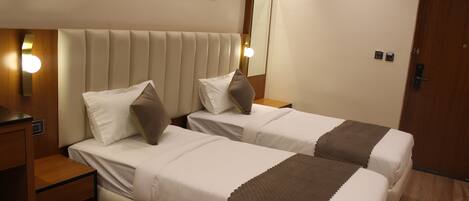 A hotel room with two beds, a wooden nightstand, a wall-mounted mirror, and a door.