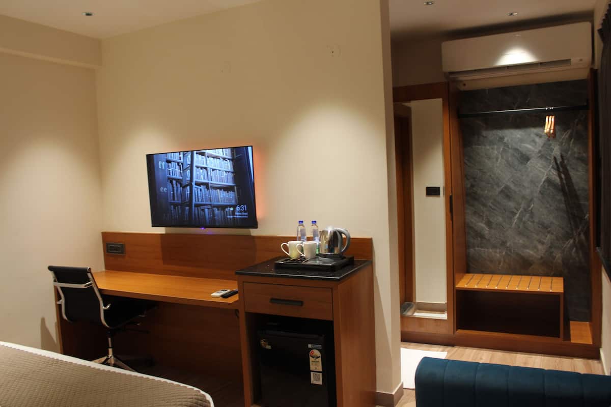 A hotel room with a wooden desk, a television, a coffee machine, and a shower area.