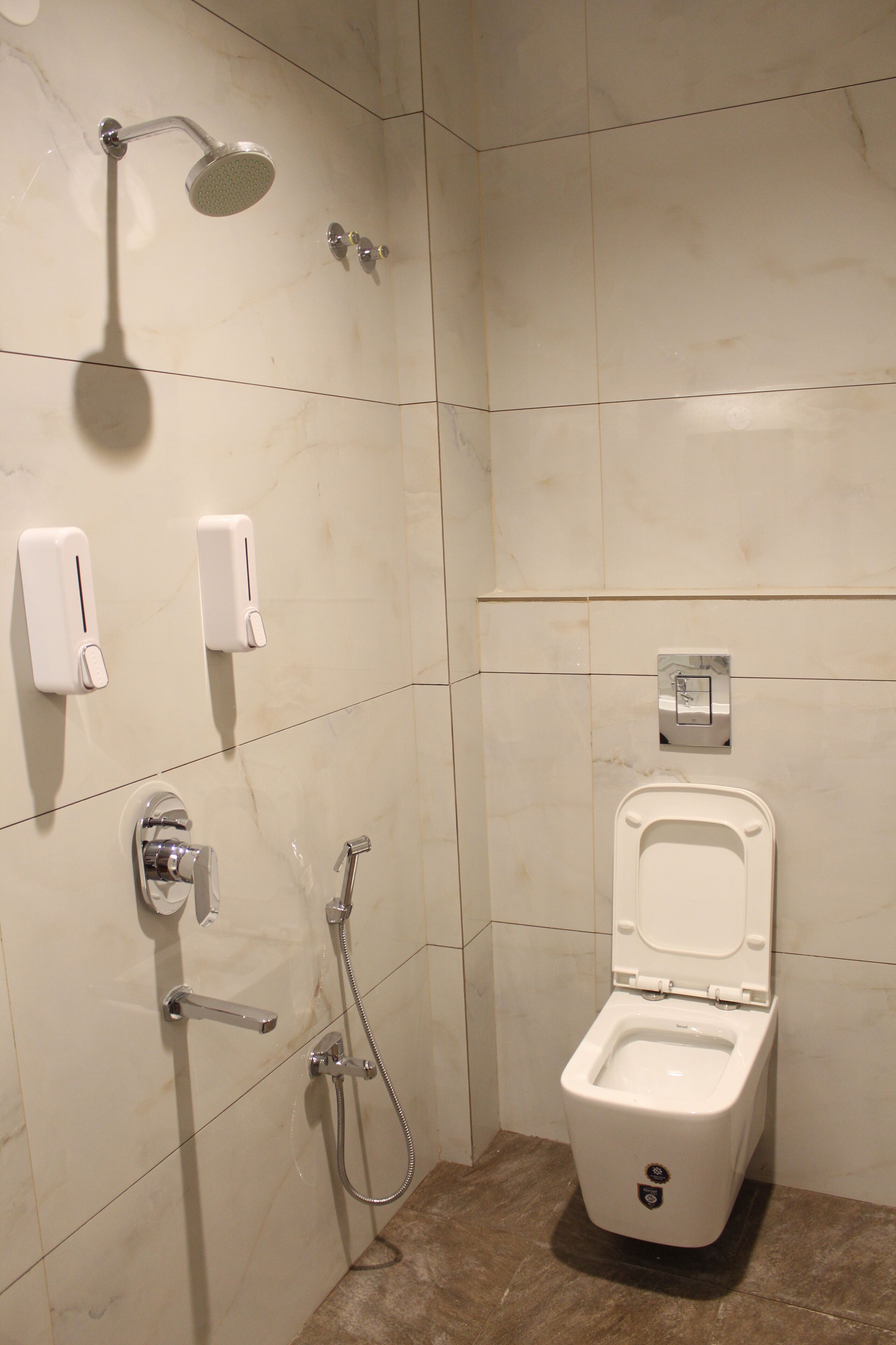 A modern bathroom with a toilet, a handheld showerhead, and a wall-mounted soap dispenser.