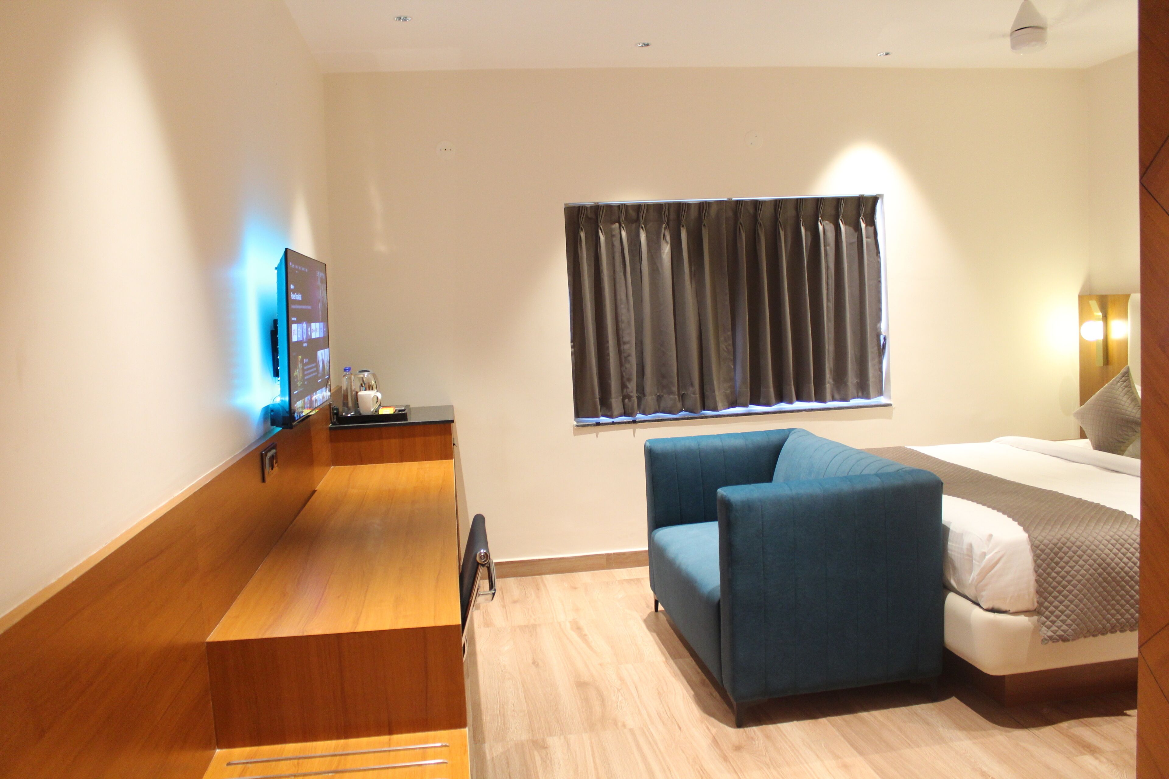 Una habitación de hotel con un escritorio de madera, un sofá azul, una cama con colchón blanco y una ventana con cortinas.