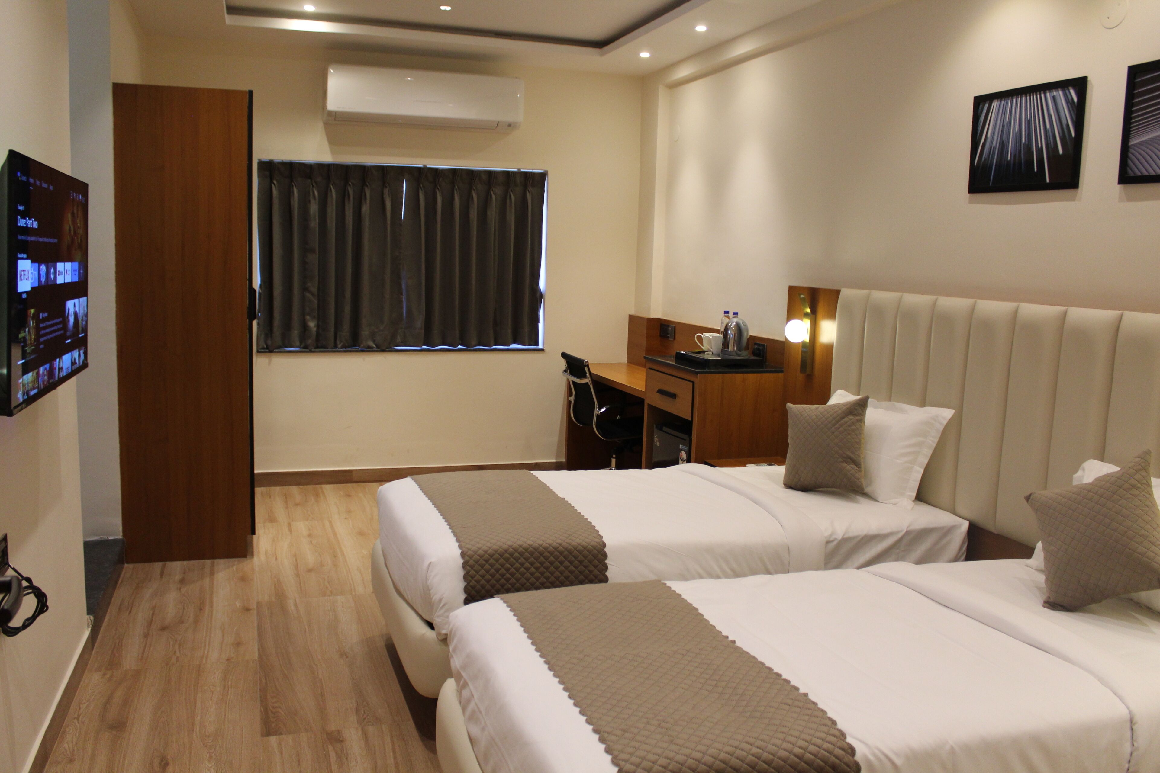 A hotel room with two beds, a desk, a chair, a TV, and a window with curtains.