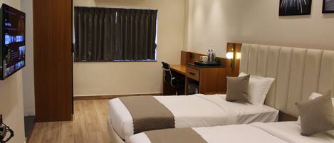A hotel room with two beds, a desk, a chair, a TV, and a window with curtains.