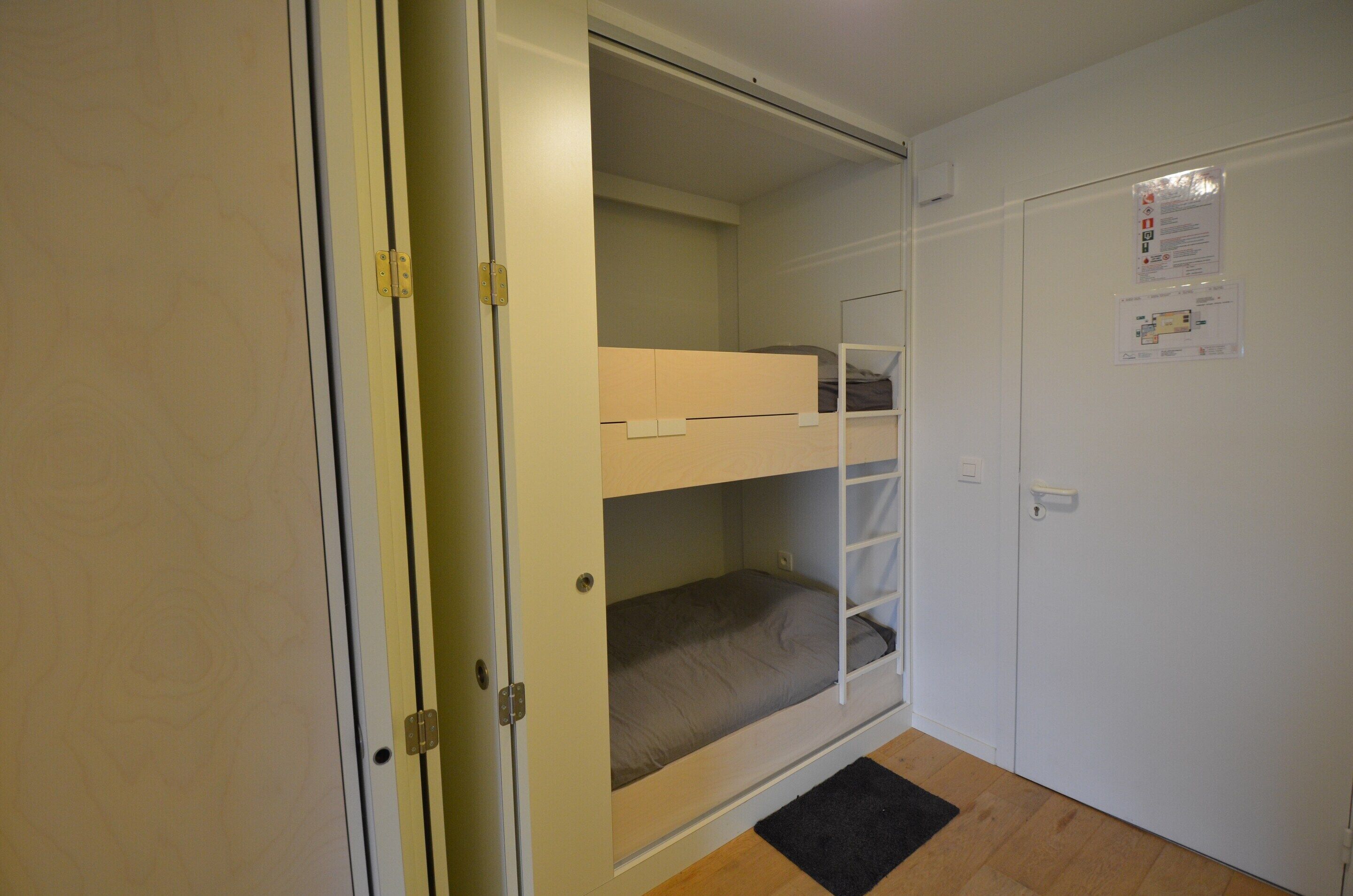 A room with a bunk bed, a door, a wall-mounted light switch, and a notice on the wall.