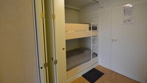 Ein Zimmer mit einem Etagenbett, einer Tür, einem an der Wand montierten Lichtschalter und einem Aushang an der Wand.
