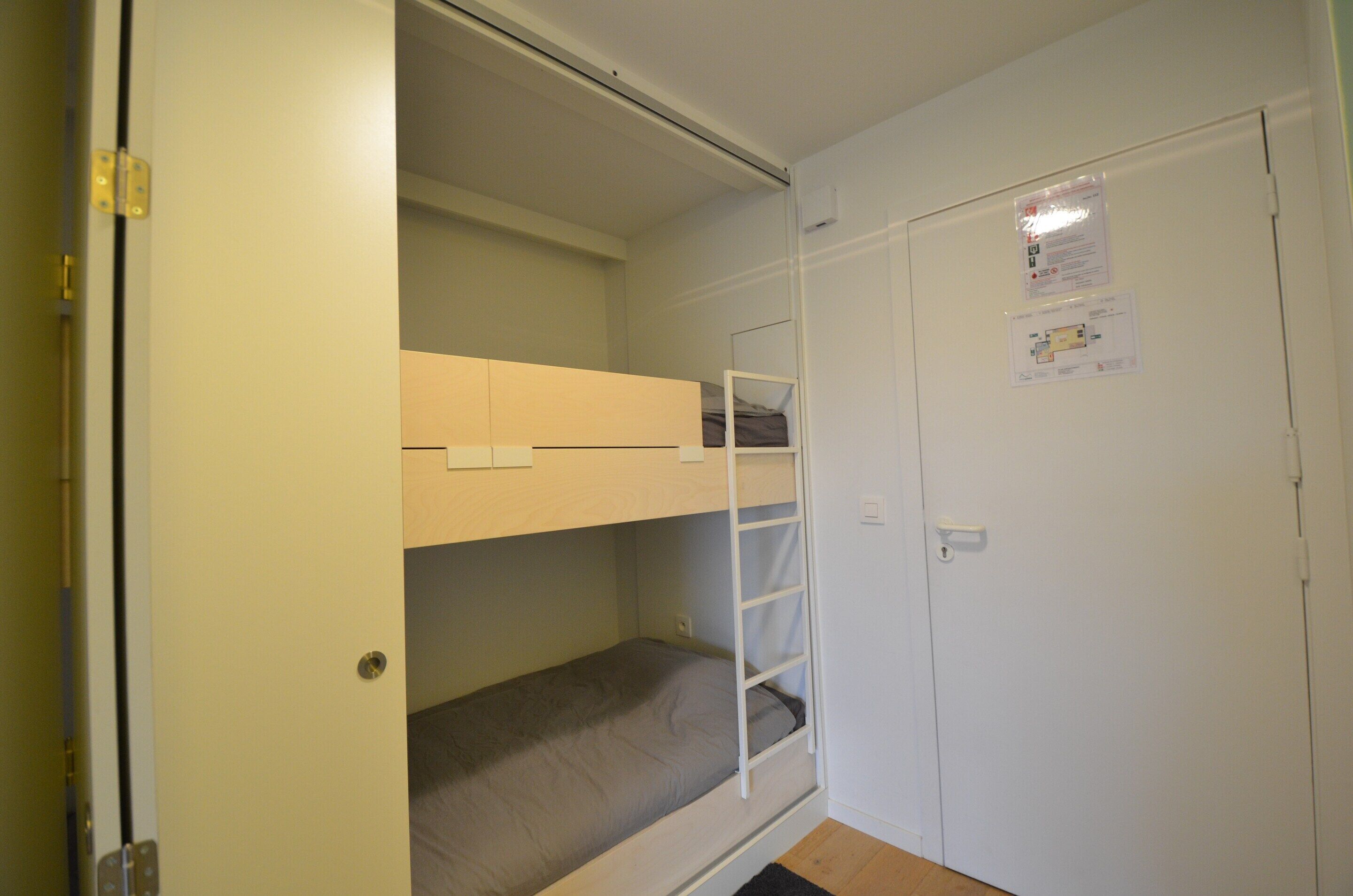 Une pièce avec un lit superposé, une porte blanche et une petite fenêtre.