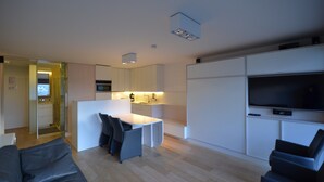 Ein modernes Wohnzimmer mit Sofa, Essbereich mit Tisch und Stühlen, Küchenzeile mit Mikrowelle und einem an der Wand befestigten Fernseher.