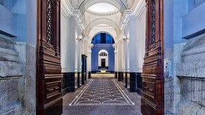 A grand hallway with a patterned floor, flanked by wooden doors and columns, leading to a central area with a blue backdrop. - Il Papero a Napoli (Naples)
