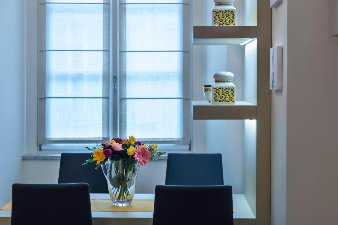 Ein Zimmer mit Esstisch, Stühlen, einer Blumenvase und Regalen mit Dekoration.
