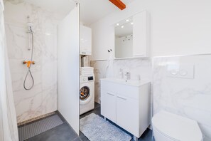 Une salle de bain moderne équipée d’une douche, d’un lave-linge et d’un lavabo blanc.