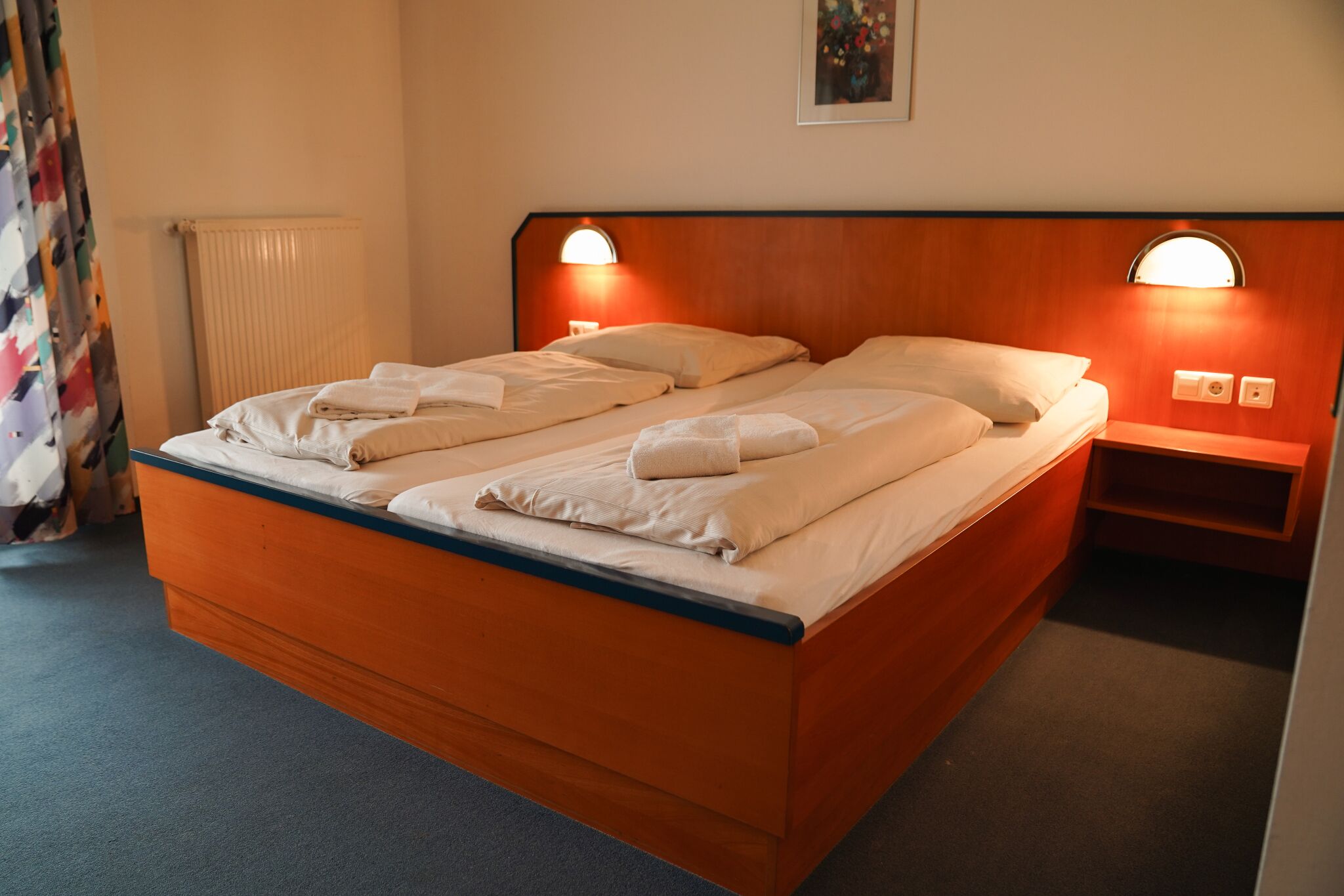 A double bed with a wooden headboard, two bedside tables with lamps, and a radiator.