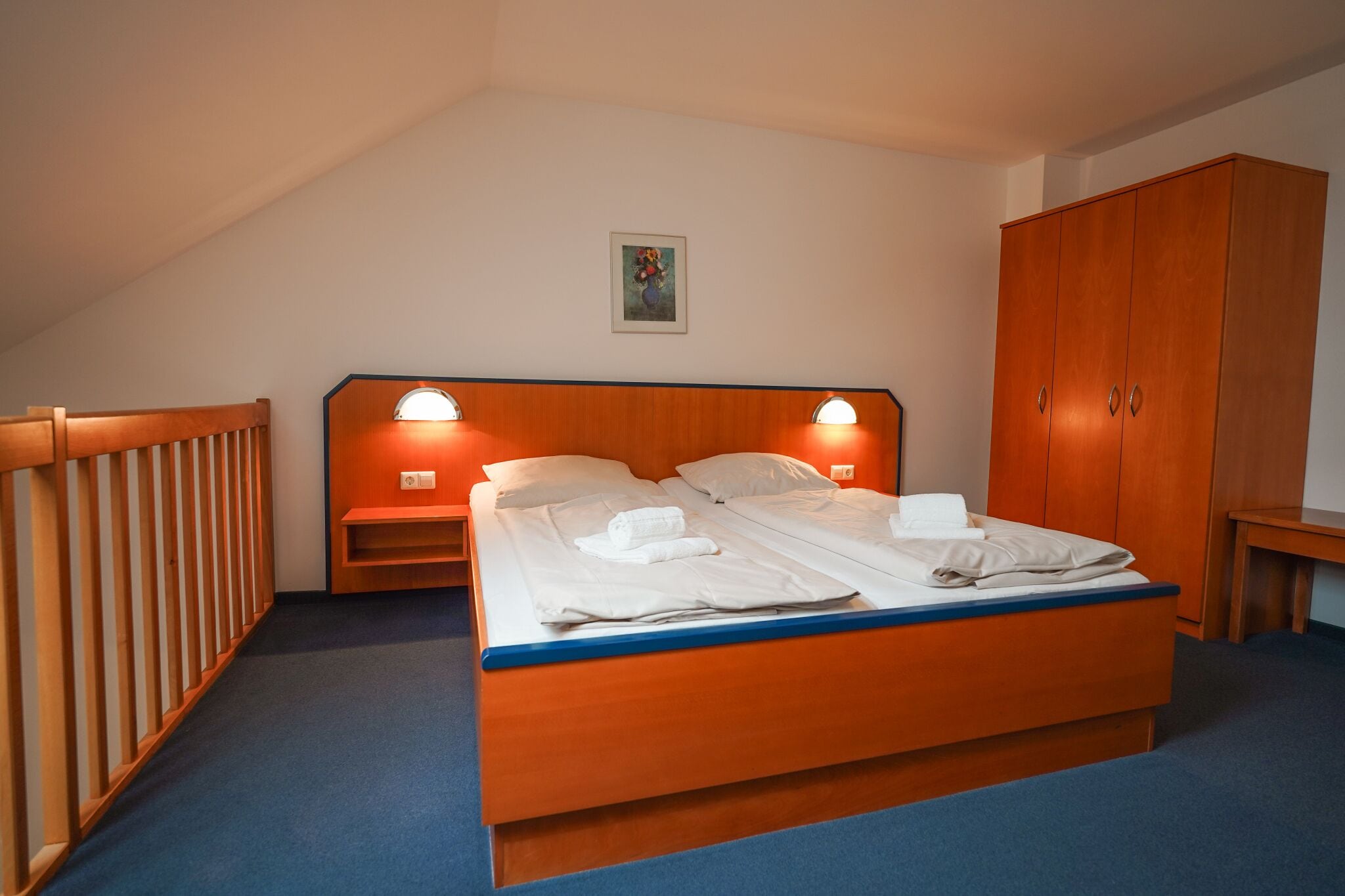 A bedroom with a wooden bed, two bedside tables, a wardrobe, and a painting on the wall.
