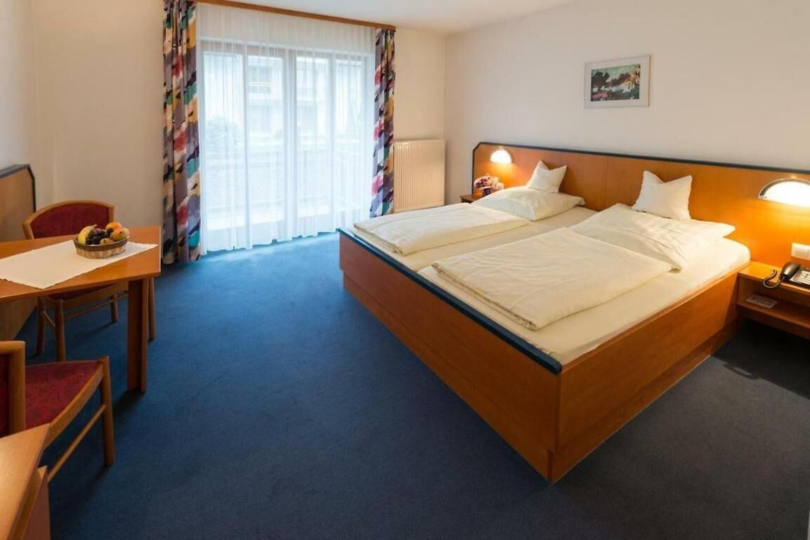 Una habitación de hotel con cama doble, un escritorio con silla y ventana con cortinas.