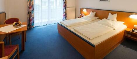 Una habitación de hotel con cama doble, un escritorio con silla y ventana con cortinas.