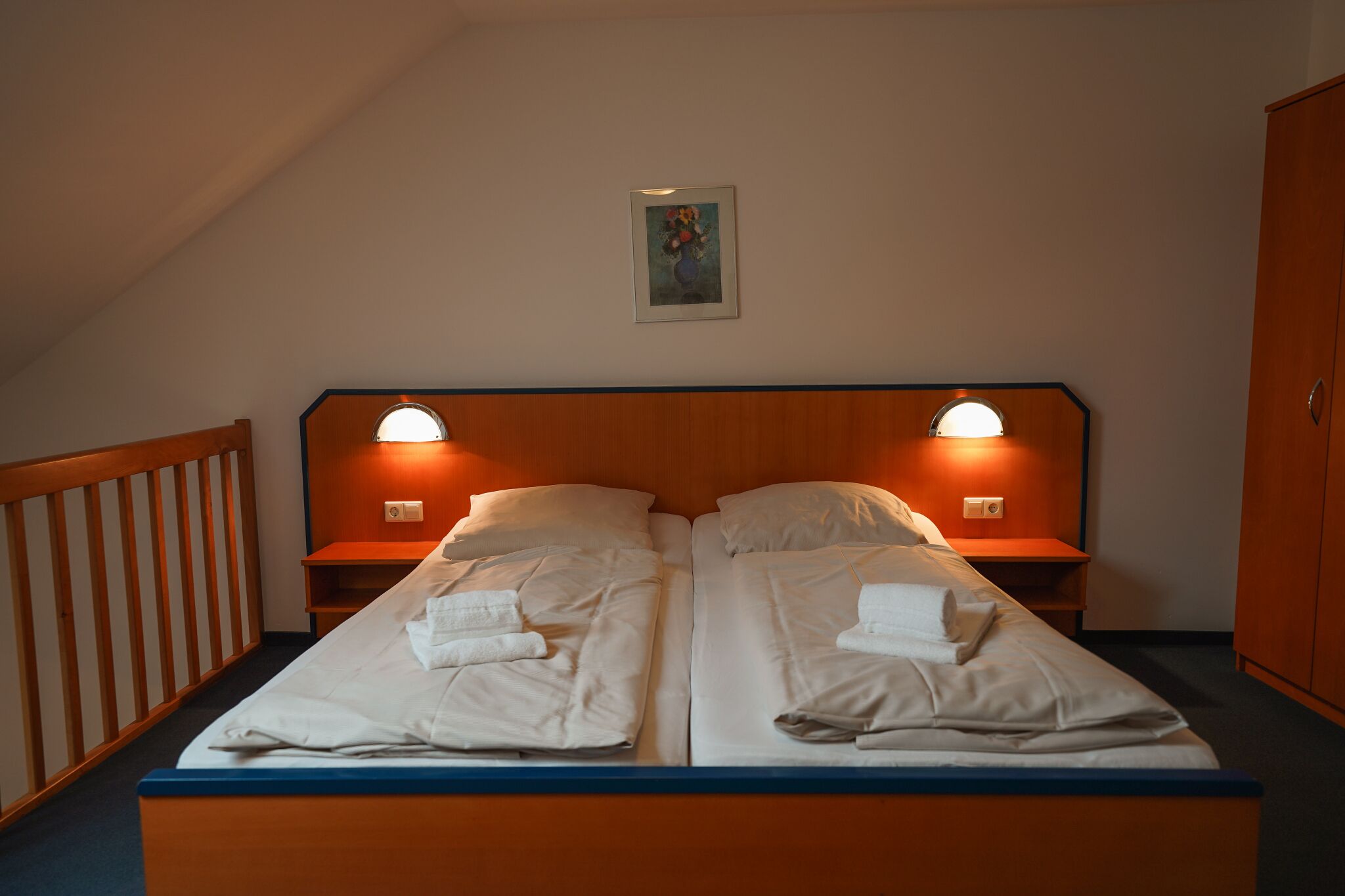 A double bed with two bedside tables, each with a lamp, in a room with a sloped ceiling and a wooden headboard.