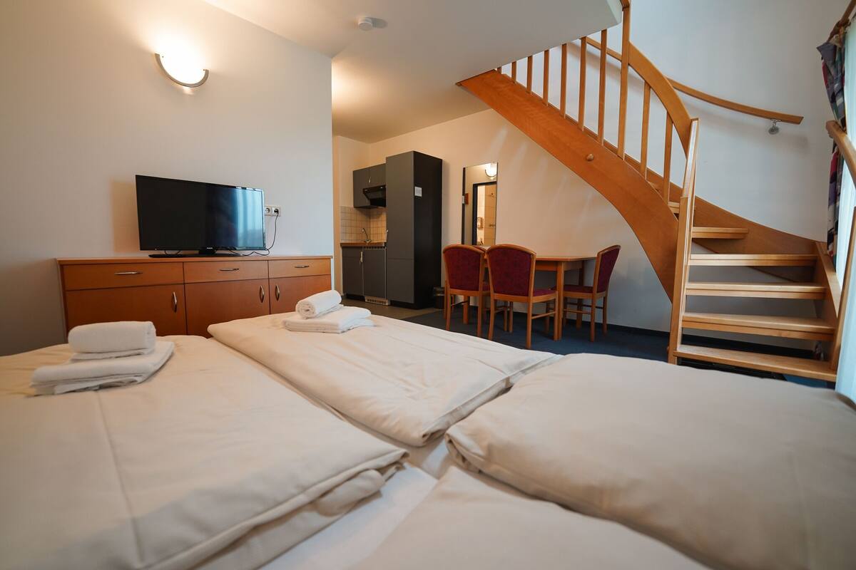 Habitación de hotel con dos camas, televisión, una escalera de madera y una pequeña cocina.