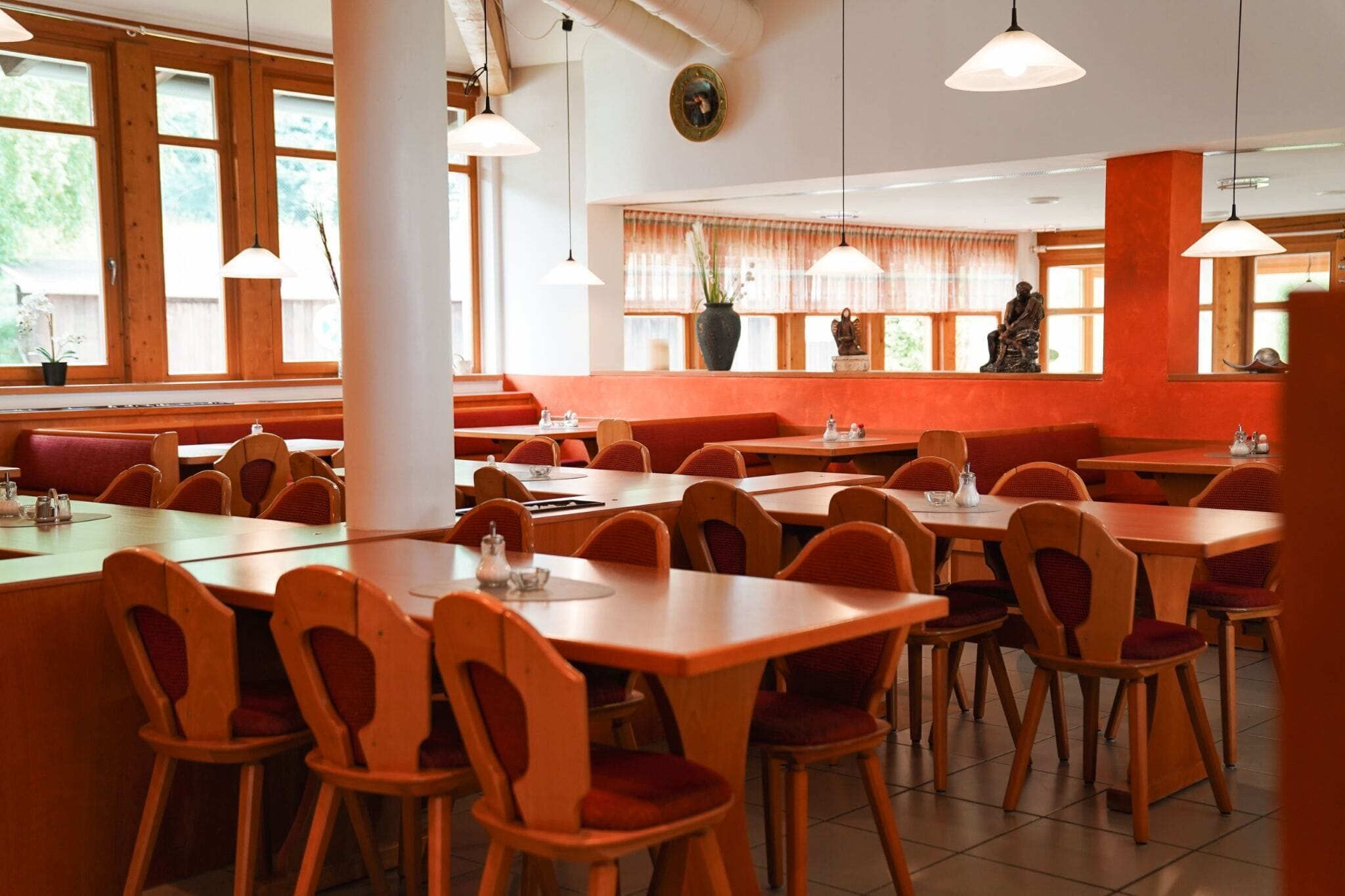 A restaurant with wooden tables and chairs, large windows, and a statue in the background.