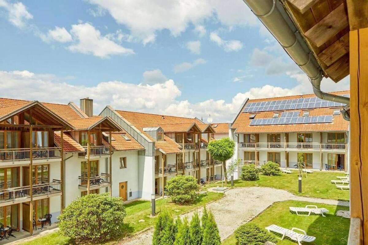 Un hotel de varios pisos con balcones, un patio con sillones de sol y paneles solares en el techo.