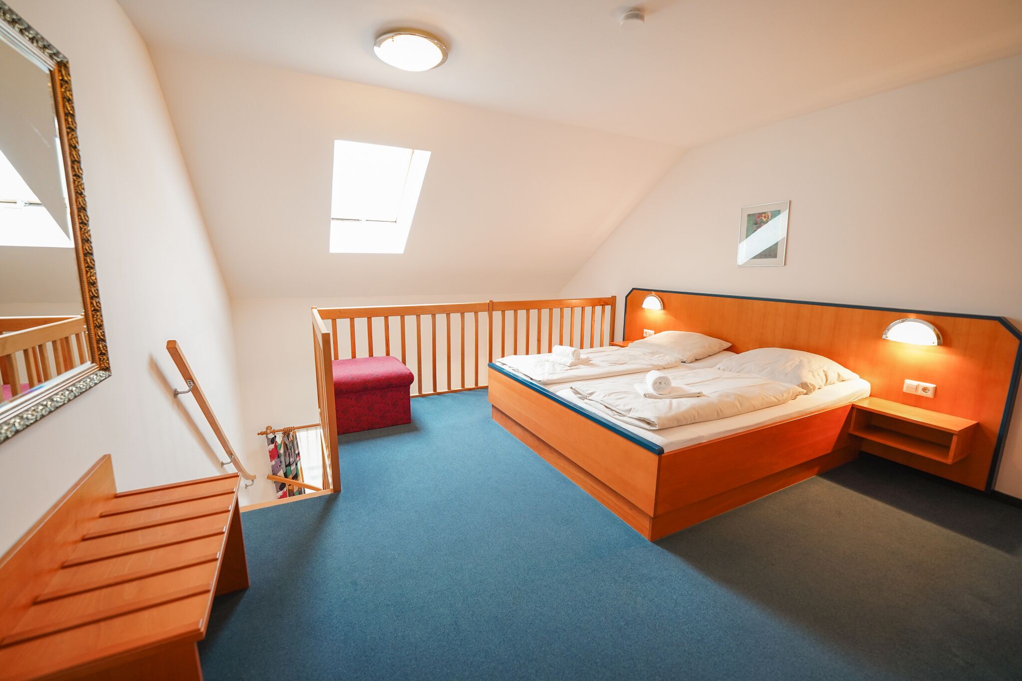 A bedroom with a wooden bed, a red bench, a mirror, and a skylight.