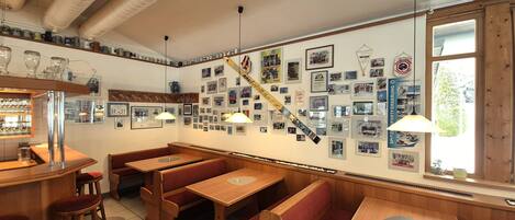 Un restaurante con bancos y mesas de madera, una pared decorada con fotos enmarcadas y un ventanal que deja entrar luz natural.