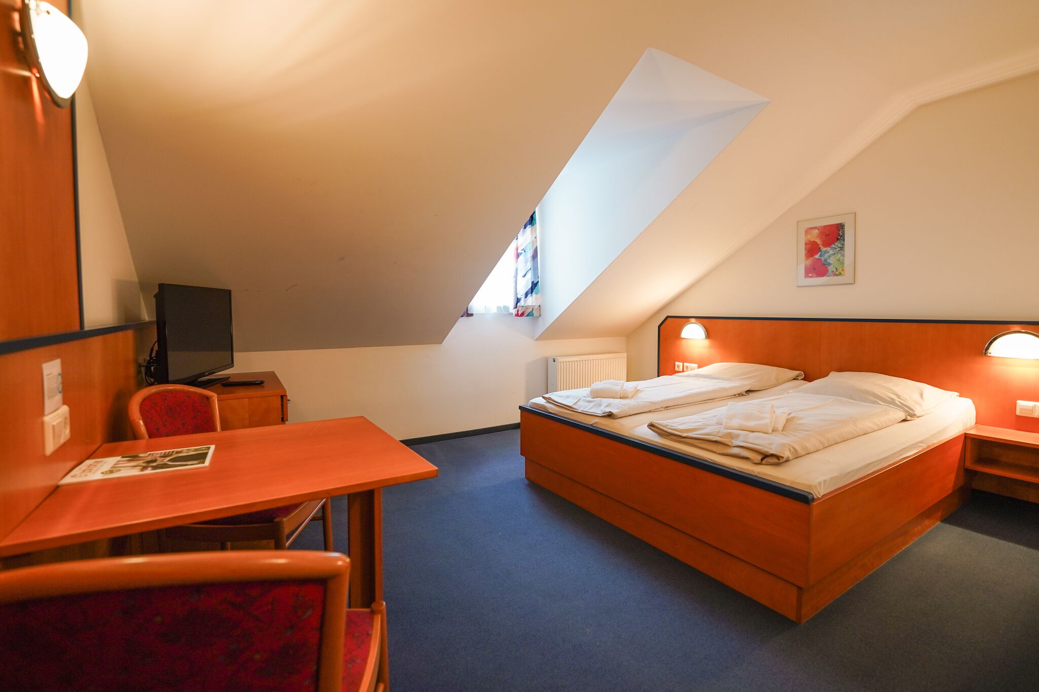 Een hotelkamer met een bed, bureau, stoel, televisie en raam.