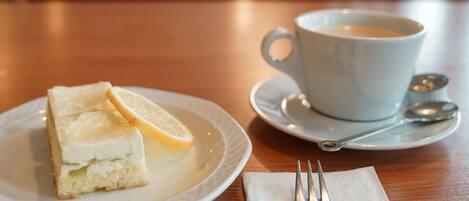 A plate with a sandwich and lemon slice, a cup of coffee, and a spoon on a table.