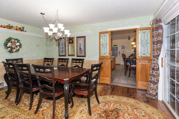 A dining room with a wooden table and chairs, a chandelier, and a patterned rug.