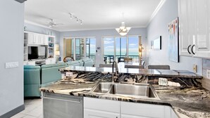Una cucina moderna con un piano di lavoro in marmo, mobili bianchi e un'ampia finestra con vista sull'oceano.