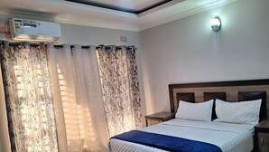 A neatly arranged bedroom with a bed, curtains, an air conditioning unit, and a nightstand. - GATOMA EXECUTIVE LODGE (Lusaka)