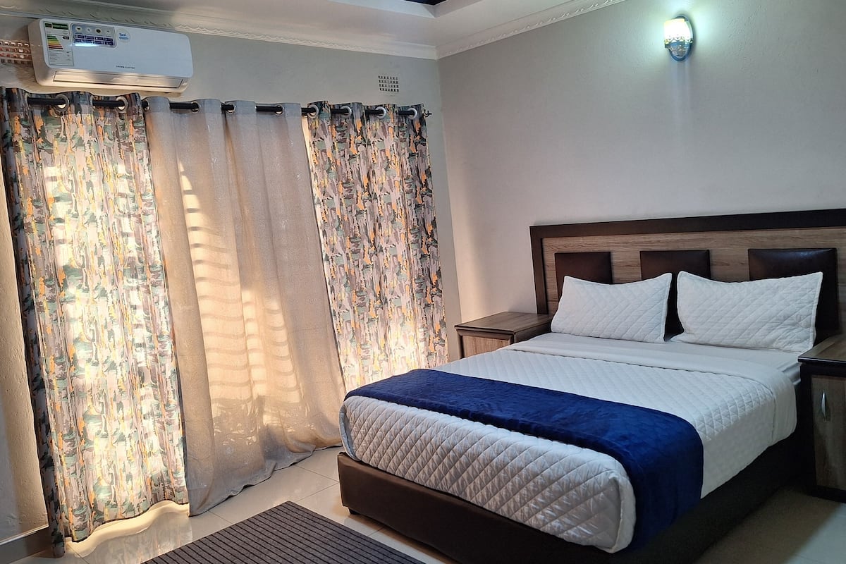 A neatly arranged bedroom with a bed, curtains, an air conditioning unit, and a nightstand.