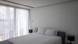 Ein modernes Hotelzimmer mit einem großen Bett, zwei Nachttischen mit Lampen, Blick auf die Stadt durch transparente Vorhänge und einem klaren, minimalistischen Design.
