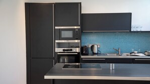 Eine moderne Küche mit schwarzen Schränken, einer eingebauten Mikrowelle, einem Backofen und einer Kücheninsel aus Edelstahl.