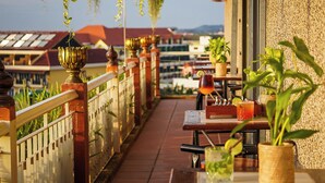 A balcony with a railing, potted plants, and a table with a drink and a menu. - Bronam Residence & Spa (Siem Reap)