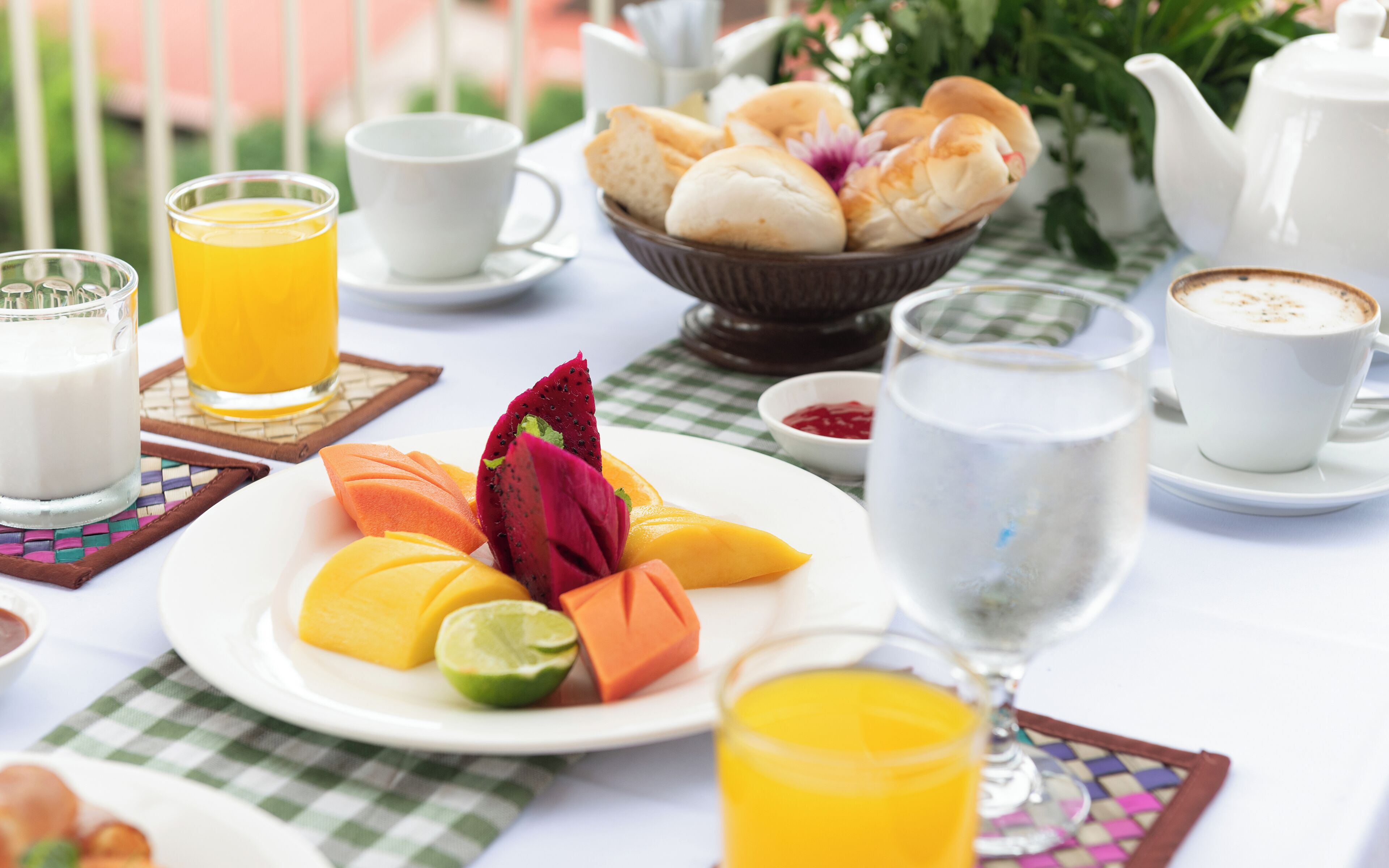 Un desayuno con una fuente de fruta, un vaso de zumo de naranja, una taza de café y un bol de pasteles.
