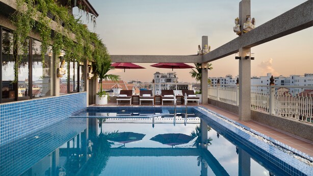 A rooftop pool with clear blue water, surrounded by lounge chairs and umbrellas, with city views in the background. - Bronam Residence & Spa (Siem Reap)