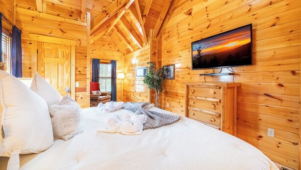 A wooden cabin bedroom with a bed, pillows, a TV, and a dresser.