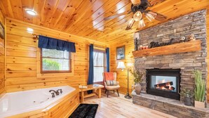 A log cabin interior with a stone fireplace, a large bathtub, and wooden walls.