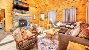 A log cabin interior with a stone fireplace, wooden furniture, and a cozy living area.