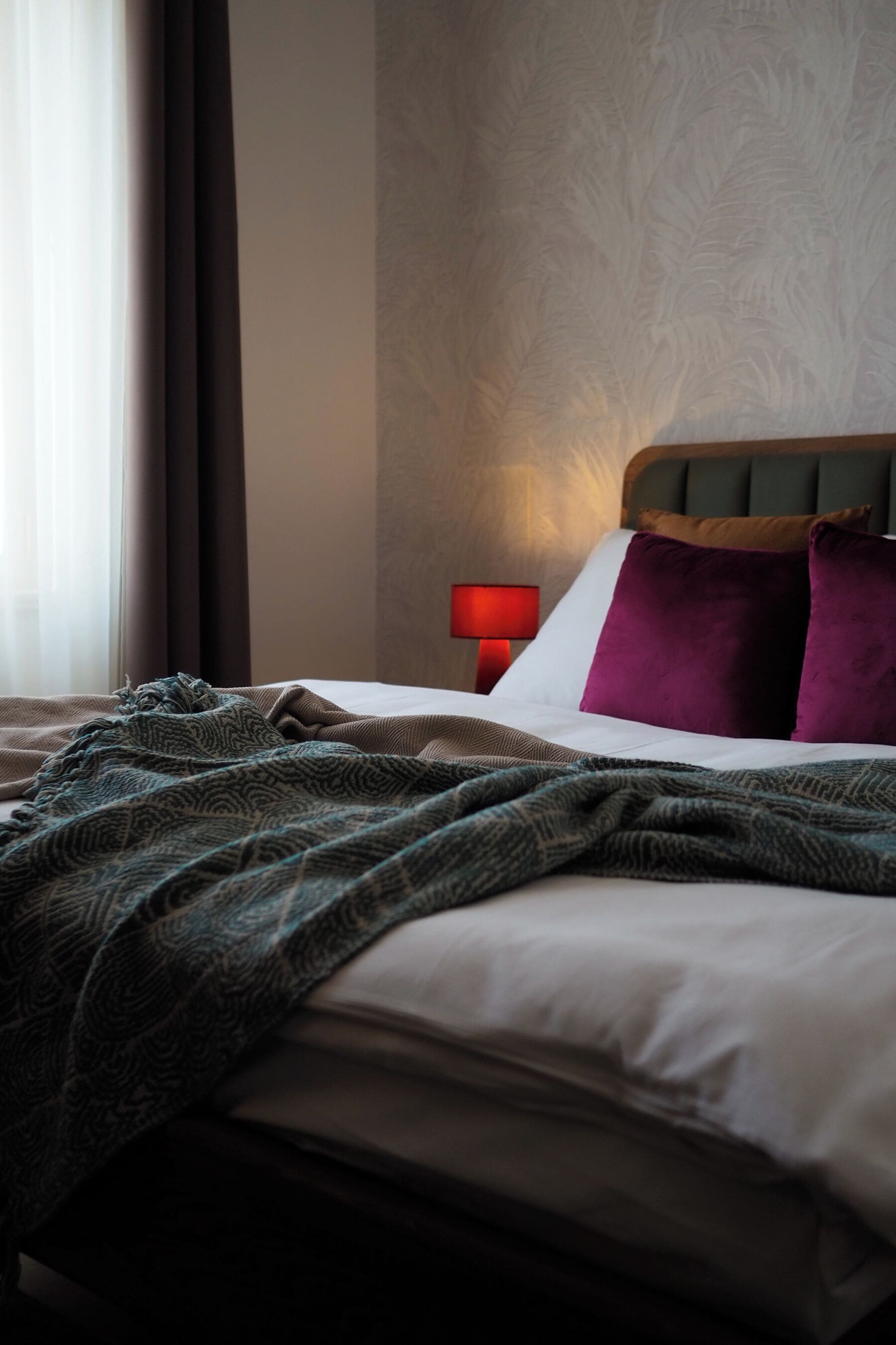 A neatly made bed with patterned blankets, a red bedside lamp, and a headboard with a textured design.