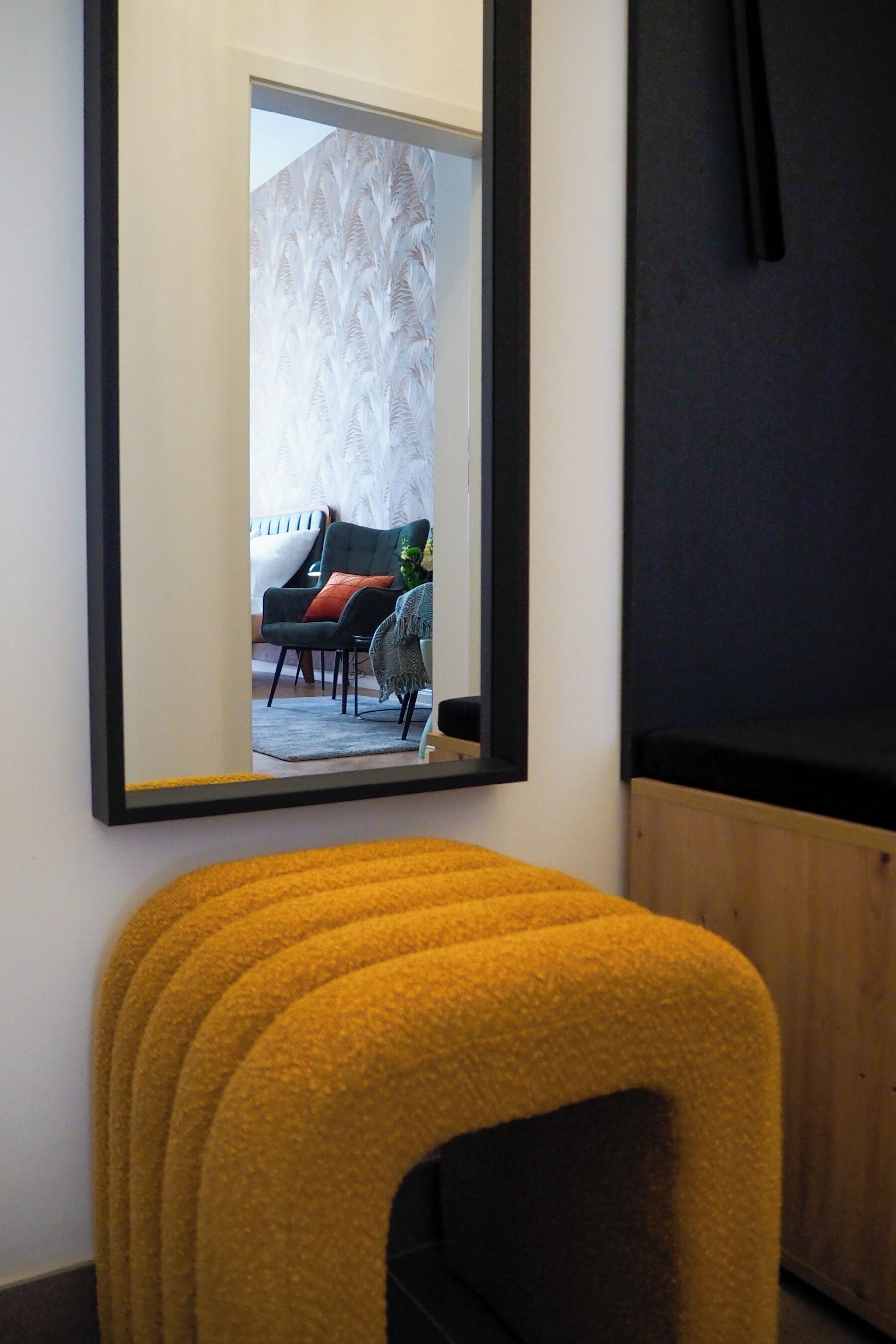 A room with a large mirror reflecting a living area with a sofa, chairs, and a table.