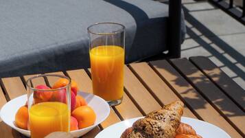 Ein Frühstück auf einer Holztischplatte mit einem Glas Orangensaft, einer Schale frischem Obst und zwei Croissants.