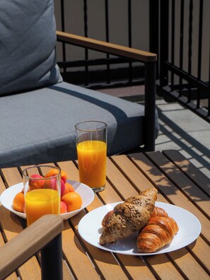 A breakfast setup on a wooden table with a glass of orange juice, a plate of fresh fruit, and two croissants.